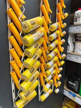 Kyiv, Ukraine - January 03, 2025: Multiple paint rollers with yellow handles placed on a display rack in a store, showcasing painting tools and equipment for home improvement tasks. clipart