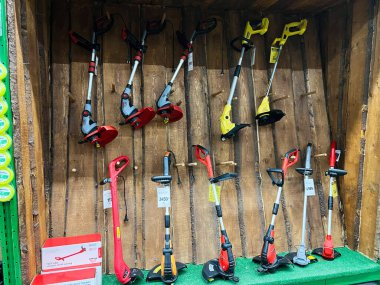 Kyiv, Ukraine - January 03, 2025: Various models of electric grass trimmers displayed in a store, organized on a rustic wooden wall. Perfect for gardening enthusiasts looking for the right tool for lawn maintenance. clipart