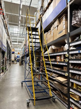 Kyiv, Ukraine - January 03, 2025: A yellow industrial ladder stands in a warehouse aisle surrounded by organized shelving units stocked with various items, boxes, and materials, illuminated by overhead lighting.