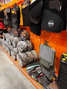 Automotive accessories including floor mats and wheel covers organized neatly on bright orange display shelving in a store aisle, showcasing a variety of branded car-related products for purchase. clipart