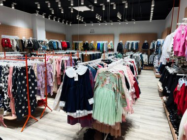 Kyiv, Ukraine - January 04, 2025: Organized clothing store featuring kids' dresses, outfits, and accessories arranged on racks under modern lighting. clipart