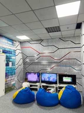 Young children relaxing on bean bags and playing video games in a vibrant, colorful, and modern entertainment and multimedia room decorated with futuristic wall patterns and equipped with several screens and consoles. clipart