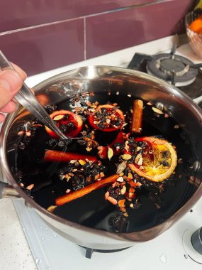 Ocağın üzerinde şarap, aromatik baharatlar, kurutulmuş meyveler ve turunçgil dilimleri bulunan bir tencere. Ev mutfağında yakalanmış mükemmel geleneksel şenlikli içecek hazırlığı..