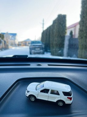 Kyiv, Ukraine - January 07, 2025: Close-up of a toy Ford Explorer SUV placed on a car dashboard, with an urban road and houses in the background, captured in bright natural lighting, combining toy photography with modern streetscape aesthetics. clipart