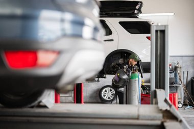 Bir araba tamirhanesinde çalışan yetenekli bir tamirci. Arabalar asansörlerde, modern bir garaj ortamında profesyonel otomotiv bakımı ve onarımı sergileniyor..