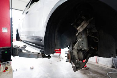 Bir atölyede asansördeki aracın yakın çekimi, tamir ve bakım için tekerlek montaj ve fren sistemine odaklanmış..