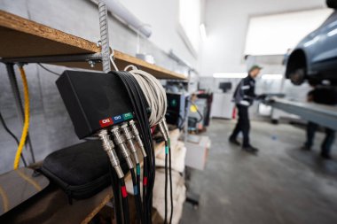 Detailed view of automotive diagnostic equipment in a mechanic's garage with technicians working on vehicles in the background. clipart