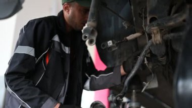 Yeşil şapkalı ve siyah eldivenli bir tamirci hidrolik asansörle yükseltilmiş bir arabanın altında çalışıyor..