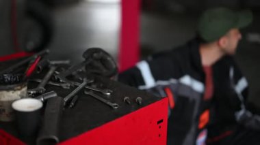 Arka planda çalışan bir tamirciyle kırmızı tezgahtaki aletleri yakın çekim yap. Çekim alanı sığ ve araçlara odaklanmış durumda..