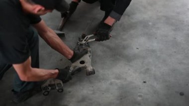 İki tamirci bir araba parçasını tamir etmek için bir garajda birlikte çalışıyorlar. Eldiven giyiyorlar ve işlerine odaklanıyorlar..