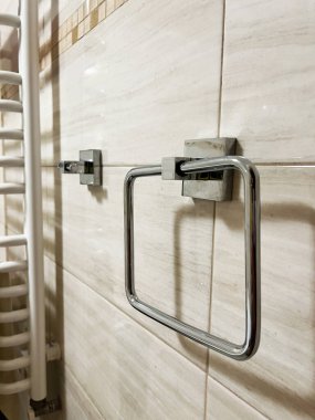 Çağdaş krom havlu tutacağı ve beyaz havlu radyatörü sergilenen fayanslı bir banyo duvarı. Genel olarak, atmosfer temiz ve çağdaş bir tasarımı yansıtır, kullanım ve gösterişli sonları vurgular..