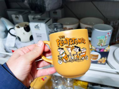 Kyiv, Ukrayna - 5 Şubat 2025: Bir mağazada sergilenen Çakmaktaşlar tasarımı içeren sarı kupayı tutan bir el.