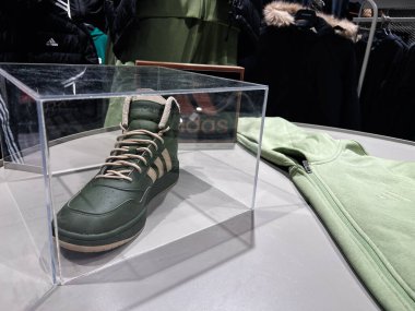 Kyiv, Ukrayna - 09 Şubat 2025: Adidas yeşil spor ayakkabısı katlanmış yeşil giysinin yanındaki şeffaf bir kutunun içinde sergilendi.