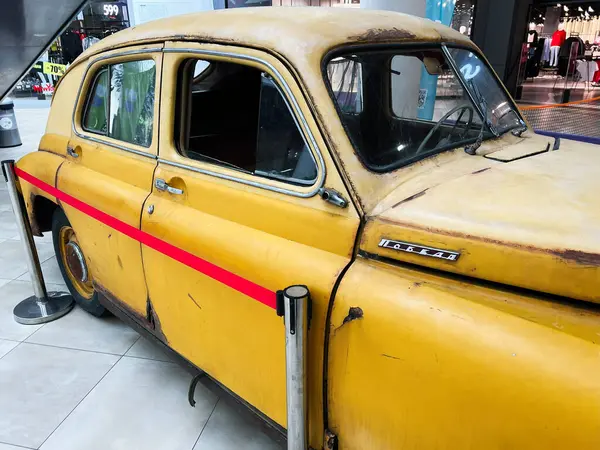 Lviv, Ukrayna - 12 Şubat 2025: Kapalı alanda klasik bir sarı GAZ-M20 Pobeda arabası, koruyucu kırmızı bariyerlerle yıpranmış cazibesini sergiliyor.