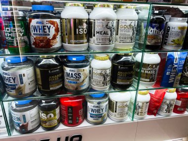 Lviv, Ukrayna - 13 Şubat 2025: Cam raflarda farklı marka ve tatlara sahip protein tozu kapları.