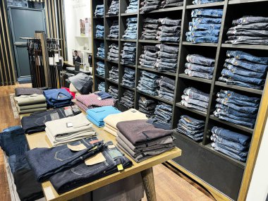 Lviv, Ukrayna - 13 Şubat 2025: Ahşap masalarda istiflenmiş kot ve günlük kıyafetlerin yer aldığı organize Bugatti perakende mağazası