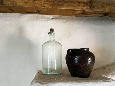 Kırsal bir taş platforma yerleştirilmiş eski bir cam şişe ve seramik sürahi..