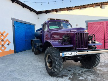 Velykyi Khodachkiv, Ukraine - February 18, 2025: Classic off-road truck ZIL-157 parked by painted gates in a courtyard under sunlight clipart