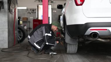 Bir otomotiv tamircisinde beyaz bir cipin lastiğini değiştirirken çekilmiş bir video. Tamirci eldiven giyiyor ve ingiliz anahtarı kullanıyor..