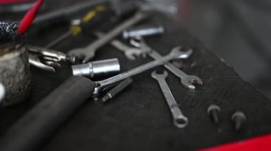 Anahtarlar, pense ve kalibreler de dahil olmak üzere çeşitli metal aletler garajdaki siyah bir tezgahta duruyordu..