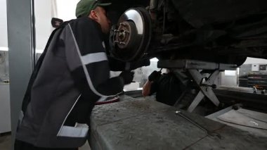 Hidrolik asansörle kaldırılan bir arabanın altında çalışan iki oto tamircisi. Profesyonel bir garajda araba tamiri yapıyorlar. Bir tamirci frenleri kontrol ediyor..