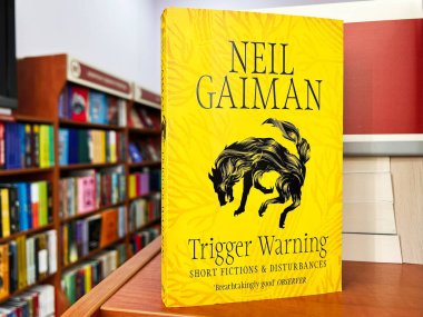 Lviv, Ukrayna - 20 Şubat 2025: Neil Gaiman, Tetik Uyarısı. Renkli kitaplarla dolu rafların üzerinde canlı sarı bir kitabın odaklanmış görüntüsü.