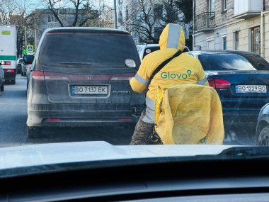 Kyiv, Ukrayna - 16 Şubat 2025: Glovo sırt çantalı bir kurye bir trafik çevirmesinde bekliyor