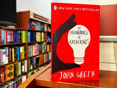 Lviv, Ukraine - February 20, 2025: A red book cover showing An Abundance of Katherines by John Green in a library setting clipart