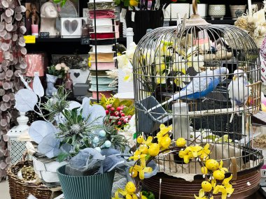 Parlak çiçekler ve pastel şeritlerle çevrili altın bir kafeste muhabbet kuşları..