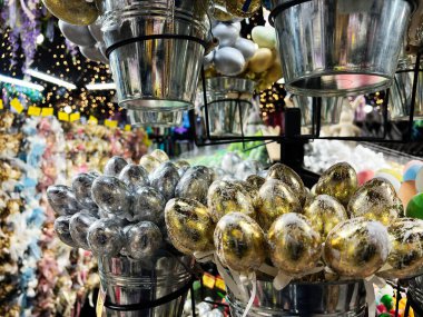 Bokeh ışıkları olan süslü bir pazarda kovalardaki parlak metalik yumurtaların yakın çekimi.
