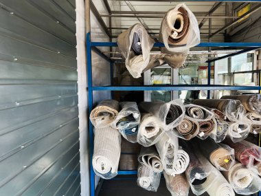 Modern bir depolama alanında sergilenen metal raflarda çeşitli kumaş ruloları var..