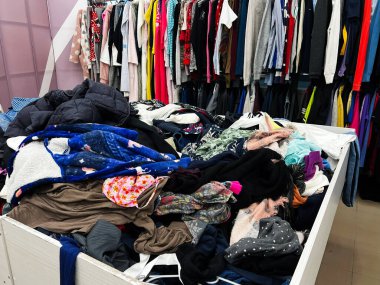 Bir perakende mağazasında asılı kıyafetlerle sergilenen karışık giysi yığınları.