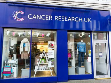 Londra, İngiltere - 2 Mart 2025: Parlak hayır kurumu mağaza vitrinleri giysi, ürün ve kanser araştırma kuruluşunu destekleyen tabela.