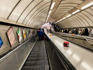 Londra, İngiltere - 02 Mart 2025: Yolcular, reklamlar ve parlak tünel aydınlatmalarıyla modern yürüyen merdiven