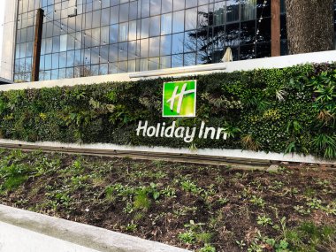 Londra, İngiltere - 02 Mart 2025: Yeşillik ve modern tasarım ile çevrili Holiday Inn tabelasıyla açık hava dikey bahçesi