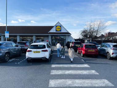 Londra, İngiltere - 02 Mart 2025: Mavi gökyüzü altında müşterileri ve araçları olan Lidl süpermarketinin önünde bir otopark.