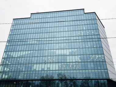 Bulutlu bir gökyüzünün altında camdan pencereleri olan çağdaş bir ofis binası.
