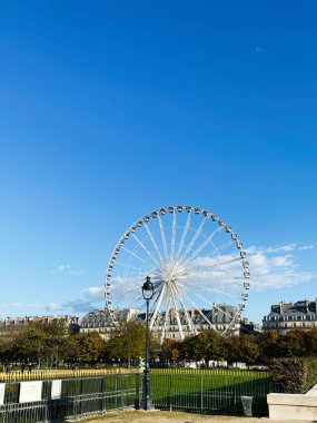 Parktaki açık mavi gökyüzüne karşı manzaralı bir Parisli dönme dolap.