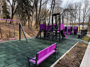 Ağaçlarla çevrili açık bir alanda mor temalı modern bir oyun alanı..