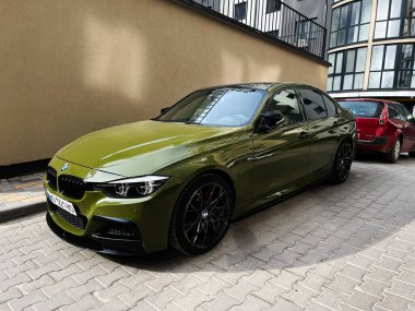 Kyiv, Ukrayna - 12 Mart 2025: Modern bir konut kompleksinin yanına park edilmiş şık yeşil BMW 3 serisi sedan araba 