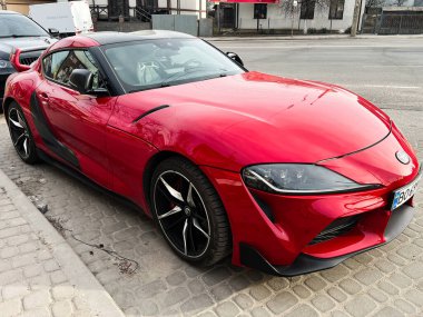 Kyiv, Ukrayna - 12 Mart 2025: Kırmızı bir Toyota GR Supra spor arabası, şık ve modern tasarımı sergilenen bir yolun yanına park edilmiş.