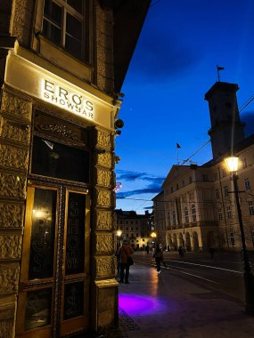 Lviv, Ukrayna - 12 Mart 2025: Aydınlatılmış Eros Showbar cephelerinin ve alacakaranlıkta aktif gece hayatının yer aldığı canlı bir şehir manzarası.