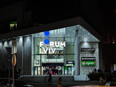Lviv, Ukrayna - 12 Mart 2025: Modern Forum Lviv alışveriş merkezi girişi geceleri birden fazla tanınabilir marka logosunun yer aldığı aydınlandı