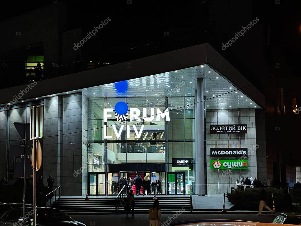 Lviv, Ukraine - March 12, 2025: Modern Forum Lviv shopping mall entrance lit up at night featuring multiple recognizable brand logos