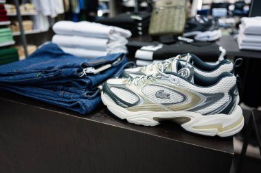 Lviv, Ukrayna - 16 Mart 2025: Beyaz Lacoste spor ayakkabıları katlanmış kot pantolonların yanına yerleştirilmiş bir mağazanın ahşap tezgahında