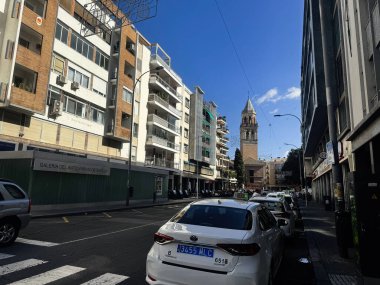 Seville, İspanya - 05 Kasım 2023 Seville, İspanya 'da şehir caddesi, kilise kulesi ve park halindeki araçlar görünür.