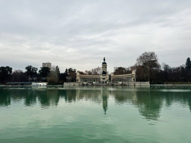 Madrid, İspanya - 28 Aralık 2023: Madrid 'deki Retiro Parkı' ndaki Alfonso XII anıtı bulutlu gökyüzünün altında yansıtıcı gölet