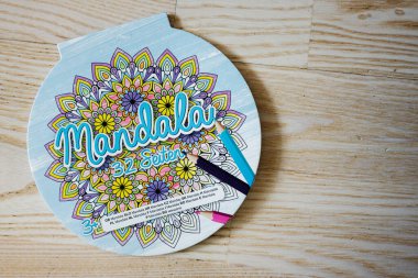 Lviv, Ukrayna - 25 Mart 2025: Mandala temalı boyama kitabı gevşemek için tahta bir yüzeye yerleştirilmiş kalemler.