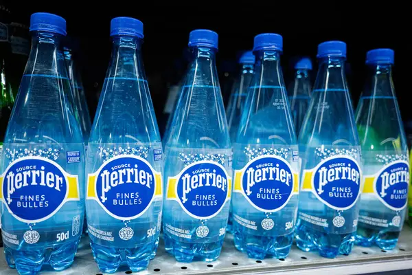 Lviv, Ukrayna - 25 Mart 2025: Parlak mavi Perrier su şişeleri mağaza ışıklarının altında düzgünce dizilmiş.
