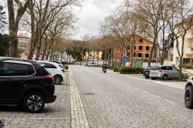 Fatima, Portekiz - 24 Mart 2025: Paved Caddesi Fatima 'da bulutlu bir gökyüzü altında araçlar ve ağaçlarla kaplı.
